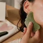 Gua sha bienfaits : pierre de jade sur le visage, main le long de la mâchoire